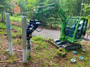 Schraubfundament mit Eindrehgerät und grünem Minibagger bei der Montage im Wald
