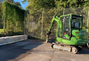 Grüner Minibagger der Morlock GmbH bei Fundamentarbeiten für eine Ballfanganlage am Sportplatz